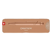 A rose gold metallic pen by Caran d'Ache, presented inside its matching rose gold metal tin packaging on a solid white background.