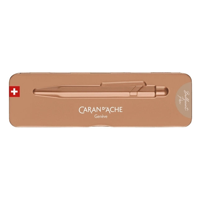 A rose gold metallic pen by Caran d'Ache, presented inside its matching rose gold metal tin packaging on a solid white background.