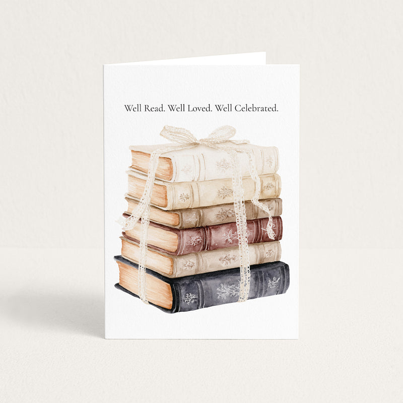 A white greeting card standing upright on a light beige background, printed with the phrase 'Well Read. Well Loved.