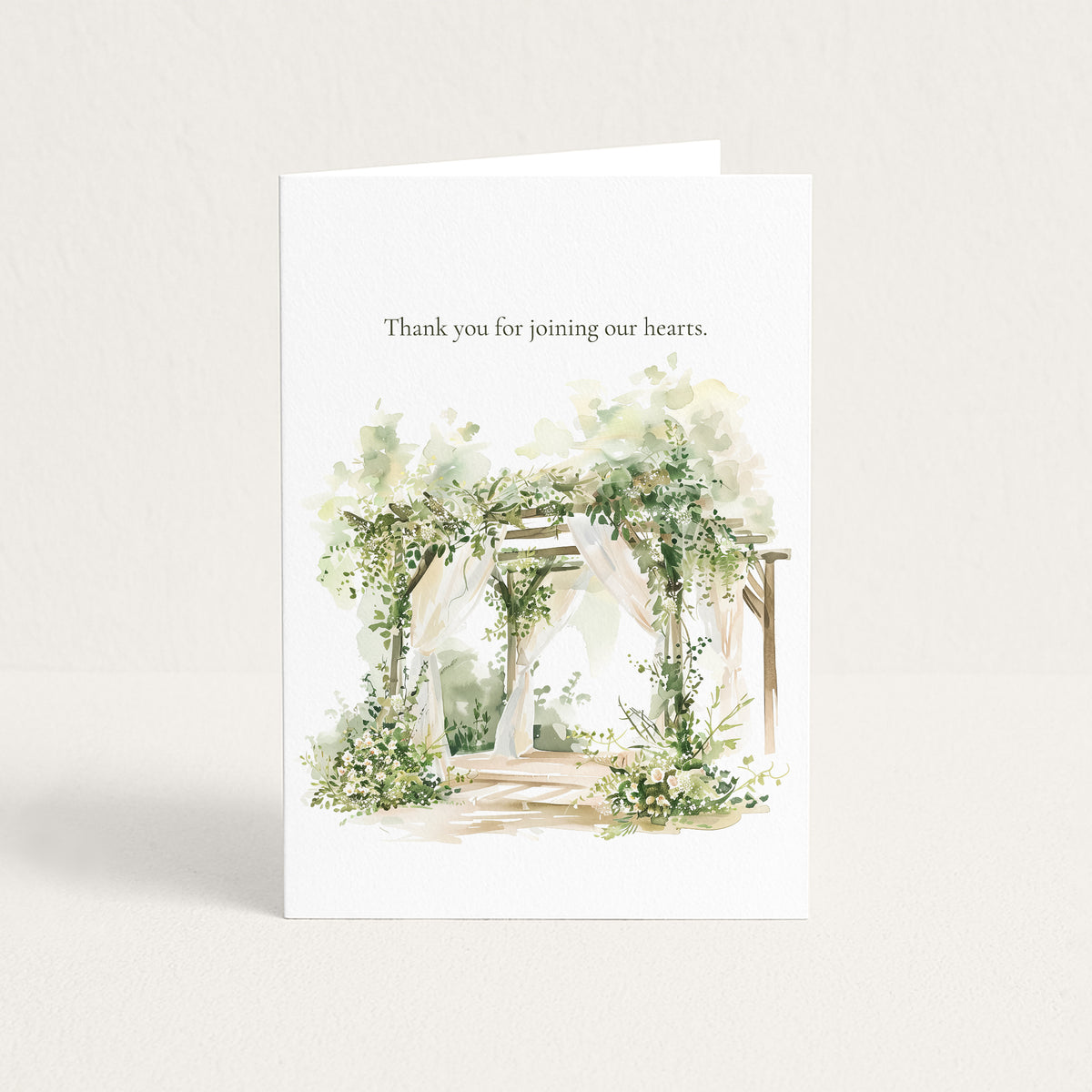 A white greeting card standing upright on a light neutral background. The card has the text 'Thank you for joining our hearts.