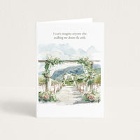 A white greeting card standing upright on a light beige surface. The card features a watercolor illustration of a wedding aisle with floral arches, chairs, and mountains in the background, with the printed text: 'I can't imagine anyone else walking me down the aisle.