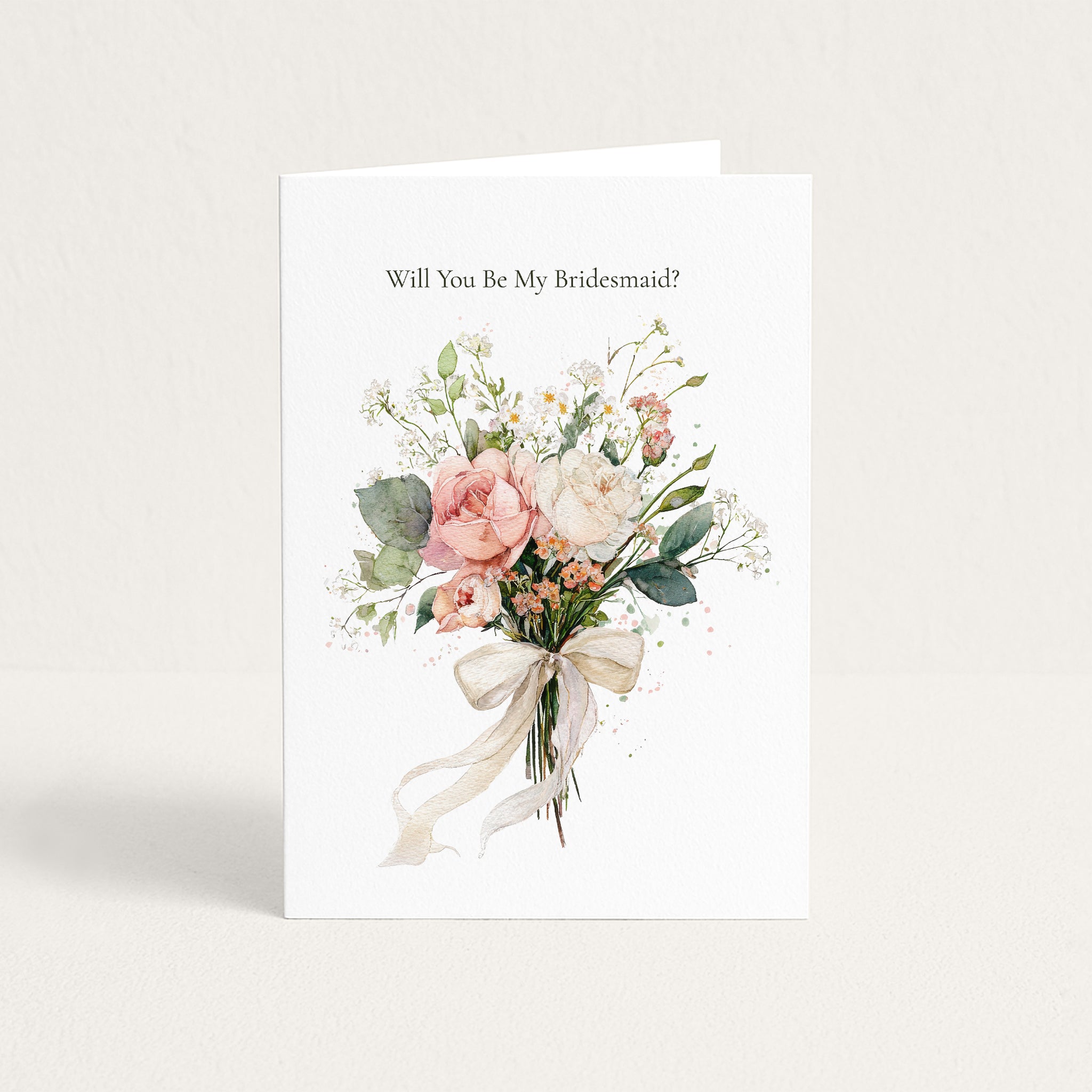 A white bridal shower or bachelorette greeting card standing upright, printed with the text 'Will You Be My Bridesmaid?' above a watercolor-style bouquet of blush pink, cream, and green flowers tied with a cream ribbon.