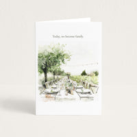 A white greeting card standing upright on a light beige background. The card features the printed text 'Today, we become family.