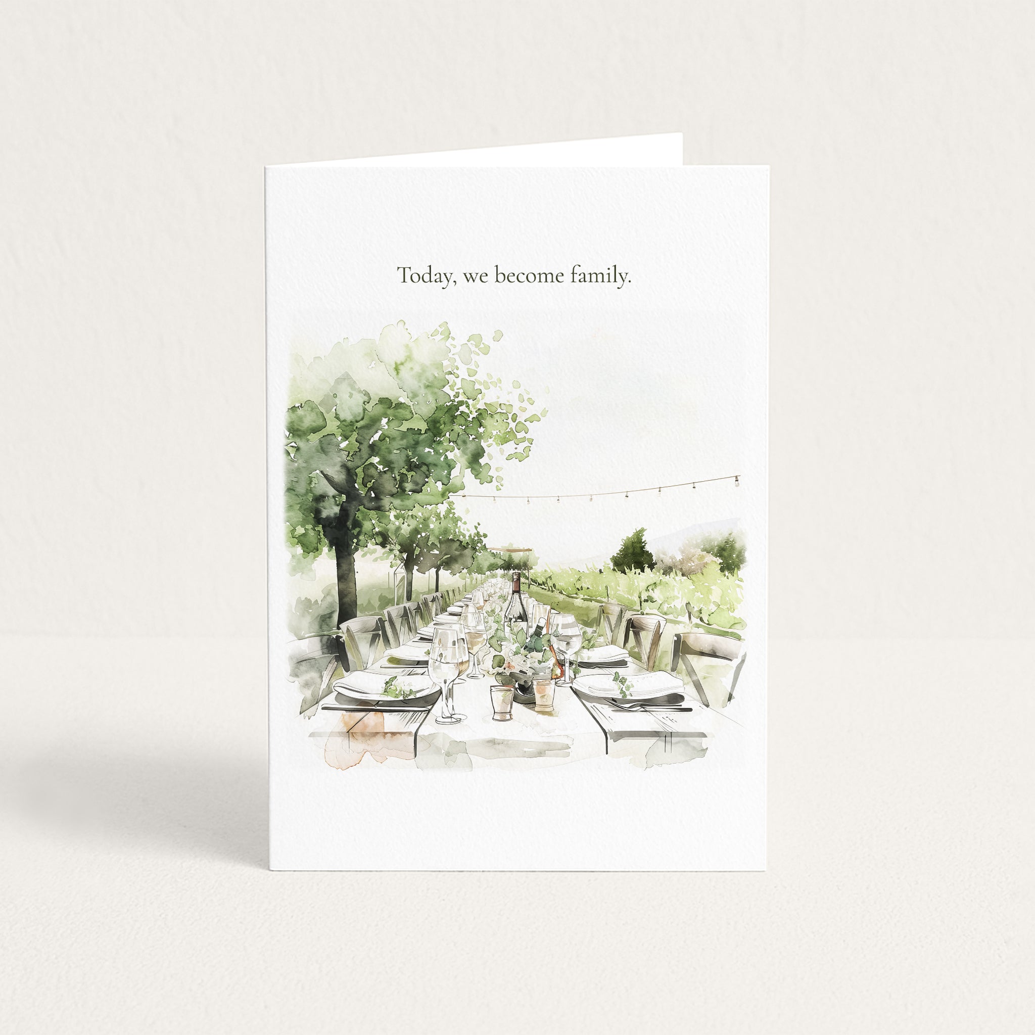 A white greeting card standing upright on a light beige background. The card features the printed text 'Today, we become family.