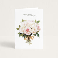 A white greeting card standing upright against a light beige background. The card features a watercolor bouquet of white and pale pink roses with green leaves and a gold ribbon, with the printed text 'Dearest Mother, on my wedding day' at the top.