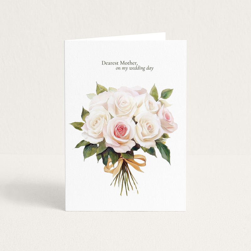 A white greeting card standing upright against a light beige background. The card features a watercolor bouquet of white and pale pink roses with green leaves and a gold ribbon, with the printed text 'Dearest Mother, on my wedding day' at the top.