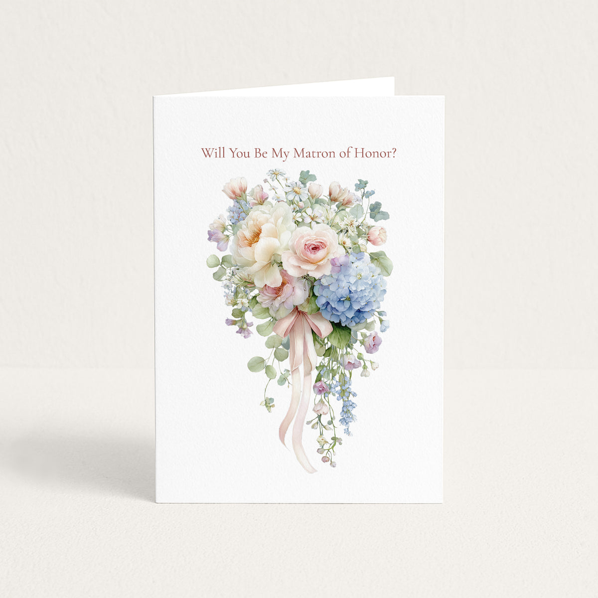 A white greeting card standing upright on a light beige surface, printed with the phrase 'Will You Be My Marron of Honor?' above a watercolor-style bouquet in soft pink, cream, blue, and green tones.