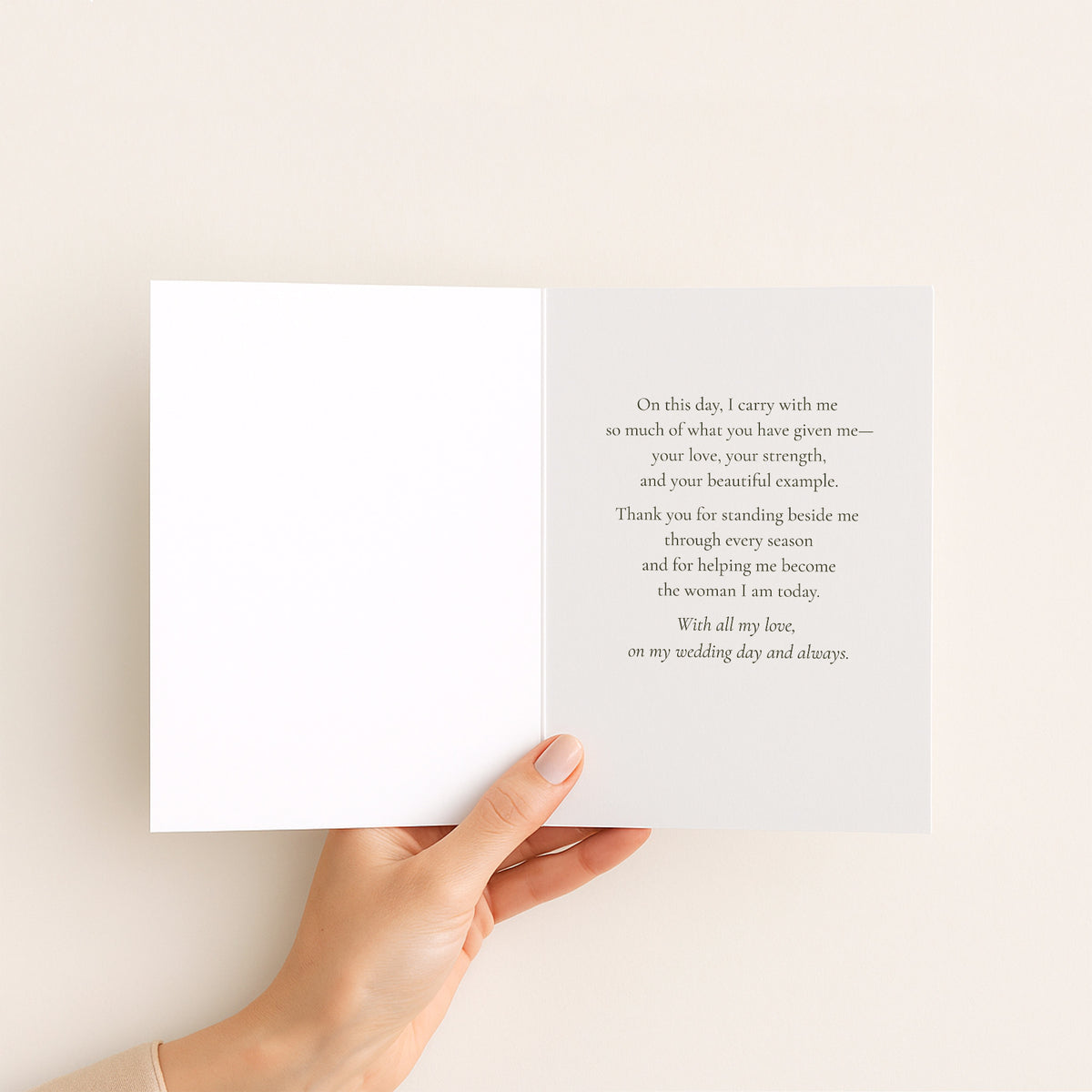 A hand holds open a white greeting card against a warm off-white background. The right page contains a printed wedding anniversary message in a small serif font.
