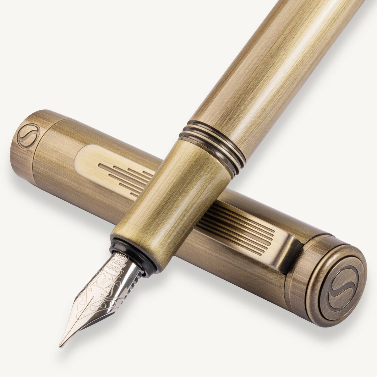 A close-up studio shot of a fountain pen and its cap in a warm metallic brass or antique gold finish, with the nib visible on the pen and a matching circular logo mark on the cap.