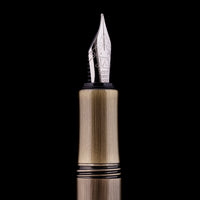 Close-up of a fountain pen nib and upper barrel against a solid black background. The nib is silver-toned with engraved lettering, and the barrel has a brushed gold/brass finish with black accent bands.