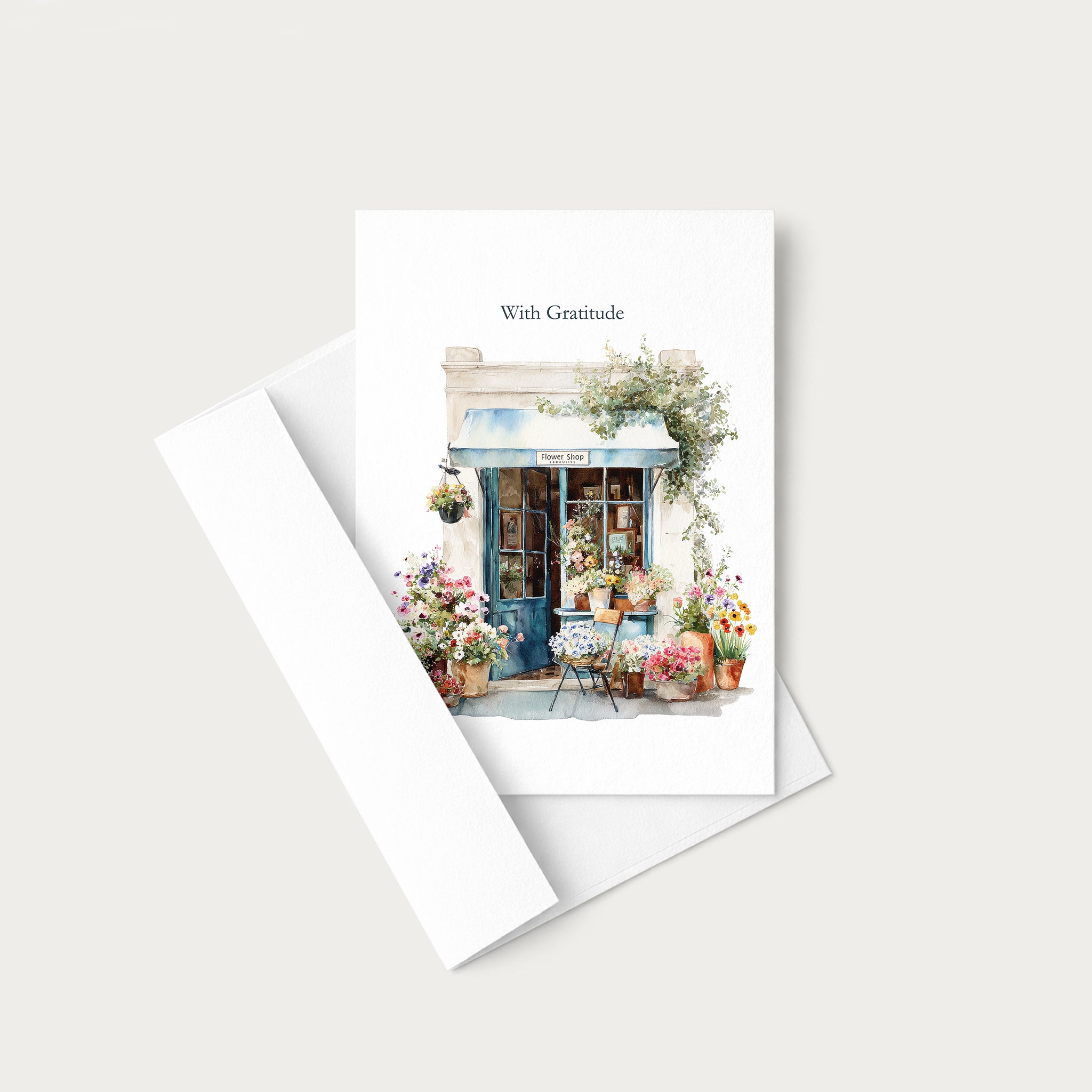 A white greeting card with a watercolor illustration of a flower shop and the text 'With Gratitude' at the top, shown with a white envelope on a light gray background.