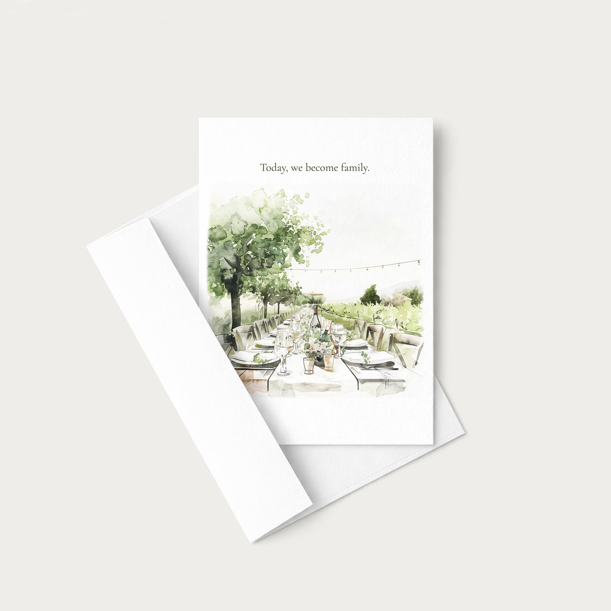 A white greeting card with a watercolor illustration of an outdoor dining scene and the printed phrase 'Today, we become family,' shown with a white envelope on a light gray background.