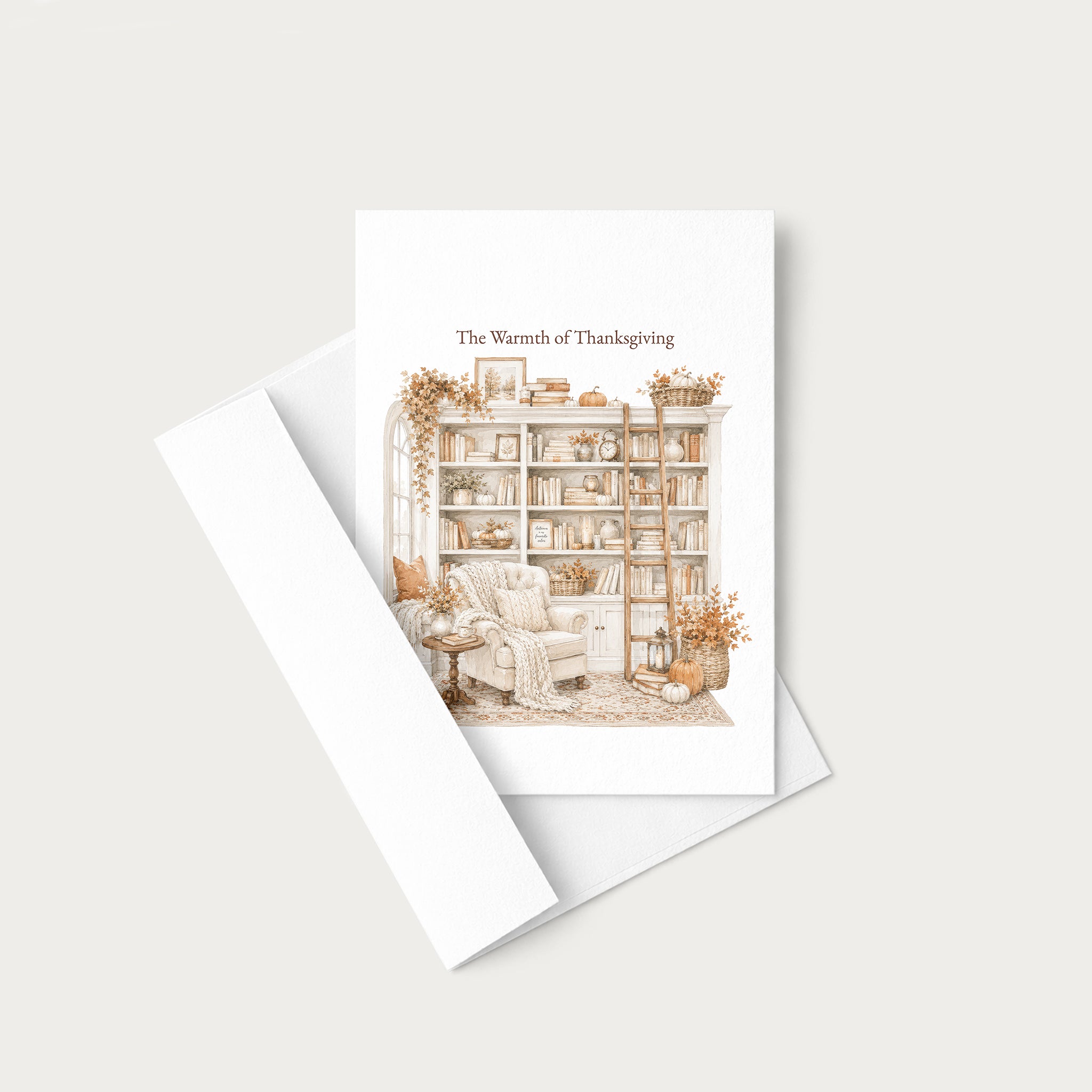 A white greeting card with the text 'The Warmth of Thanksgiving' and a delicate illustration of a cozy reading nook with a bookshelf, armchair, and autumn decor, shown with a white envelope on a light beige background.