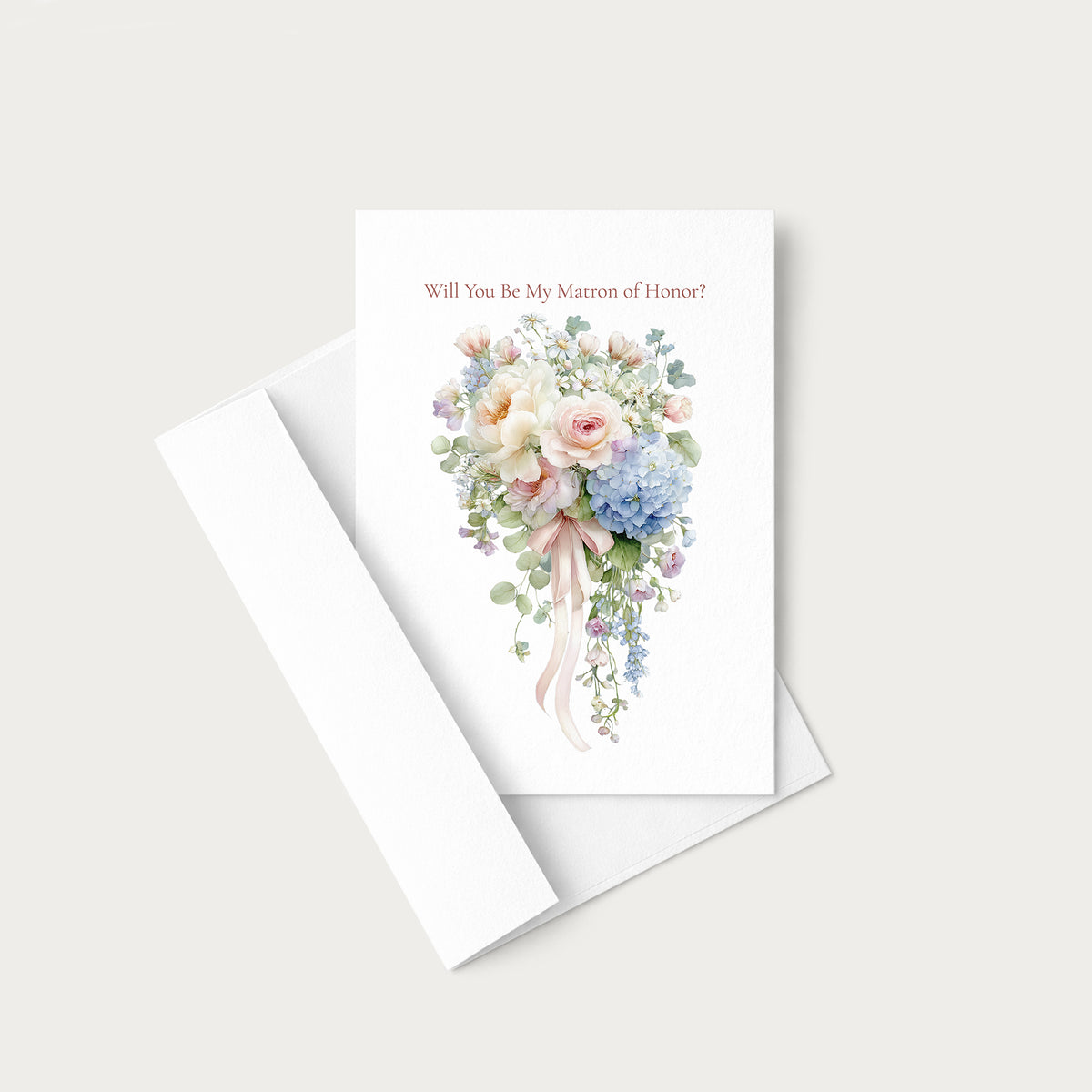 A white wedding greeting card with a watercolor bouquet illustration and the printed phrase 'Will You Be My Mateon of Honor?' in dusty pink, shown with a white envelope on a light warm-gray background.