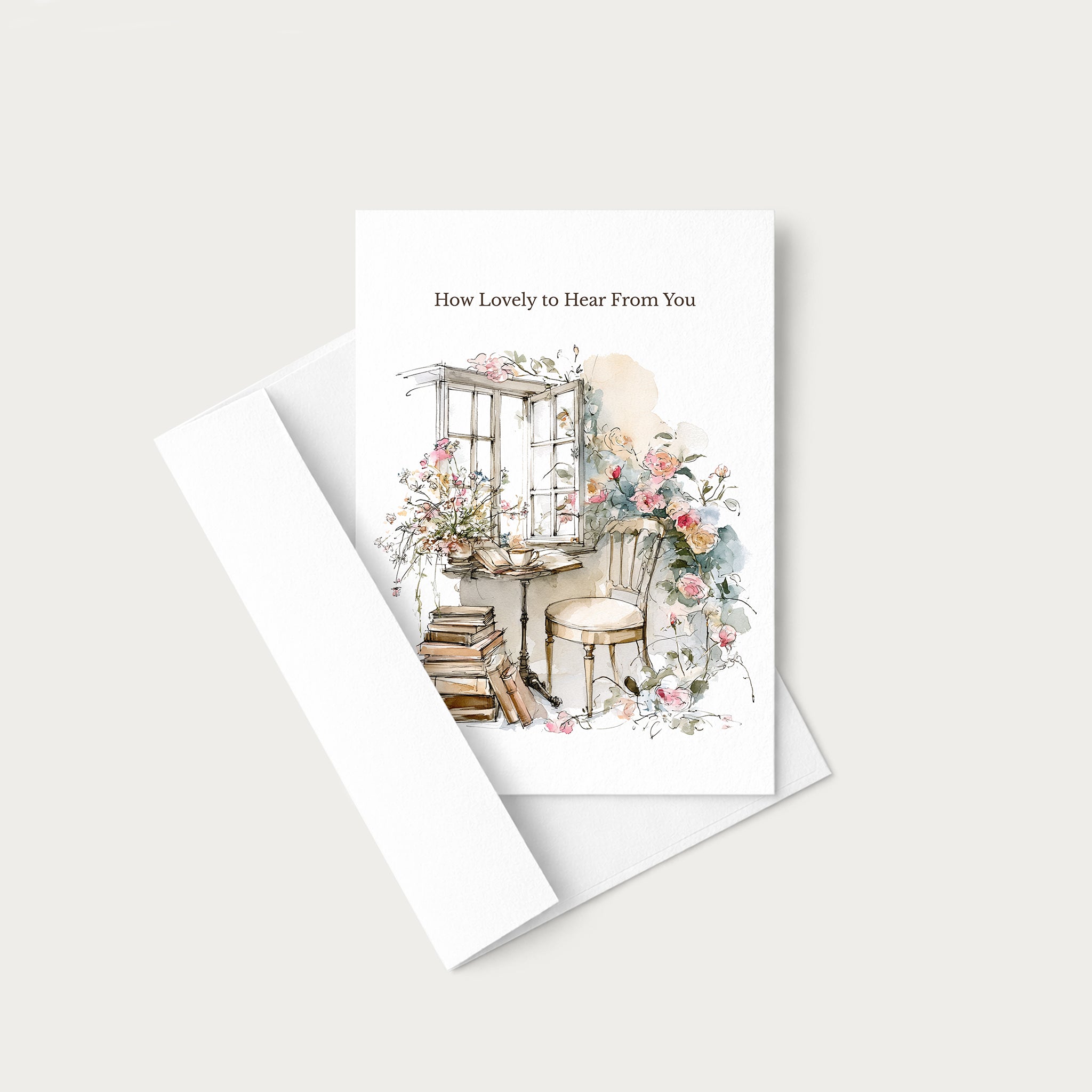 A white greeting card with a watercolor illustration of a cozy interior scene and the text 'How Lovely to Hear From You,' shown with a matching white envelope on a light neutral background.