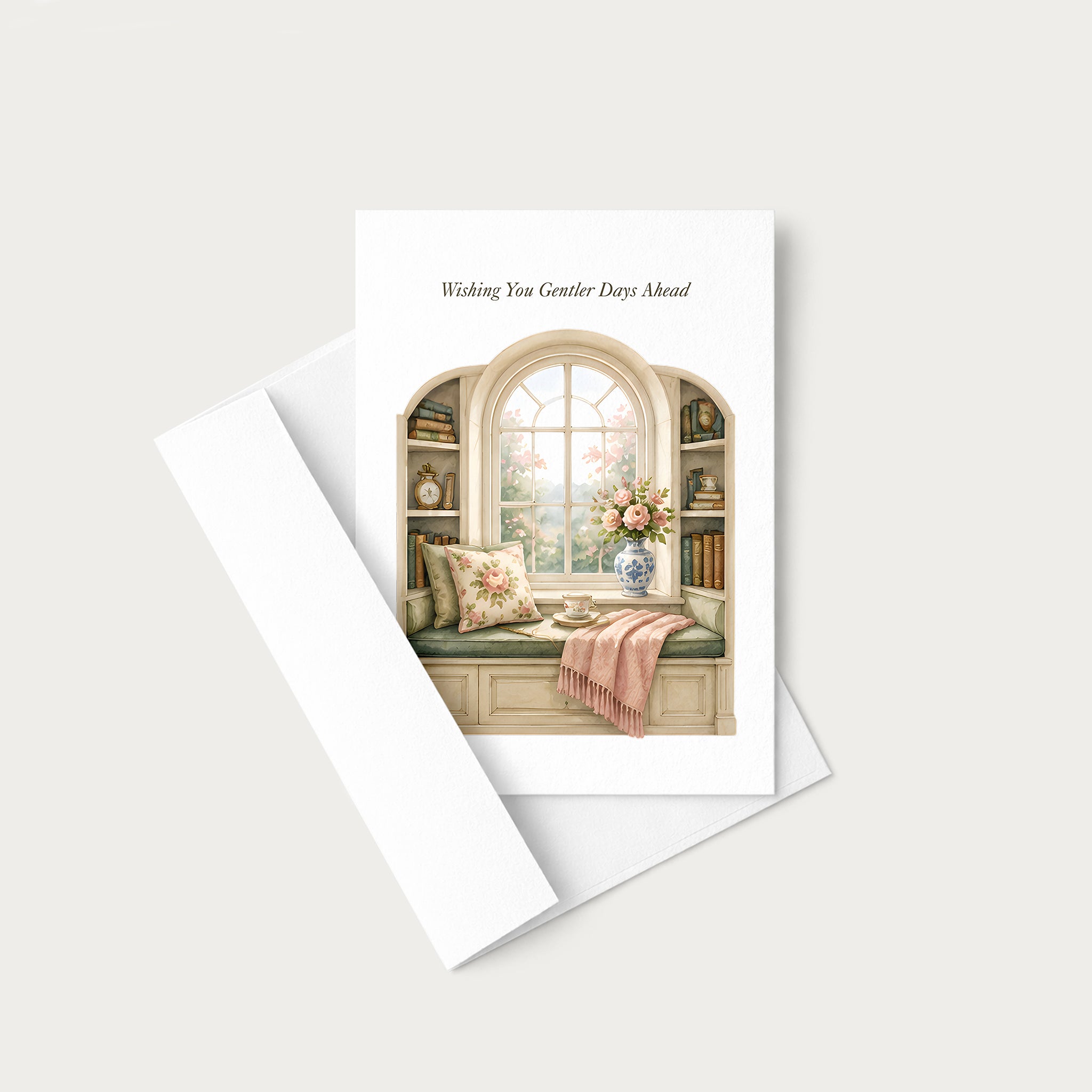 A greeting card with a white envelope, featuring an illustration of a cozy window seat with flowers and a pink throw blanket, with the text 'Wishing You Greater Days Ahead' printed at the top.