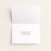 A white greeting card shown open against a light beige background, with a small centered black text message on the lower half.