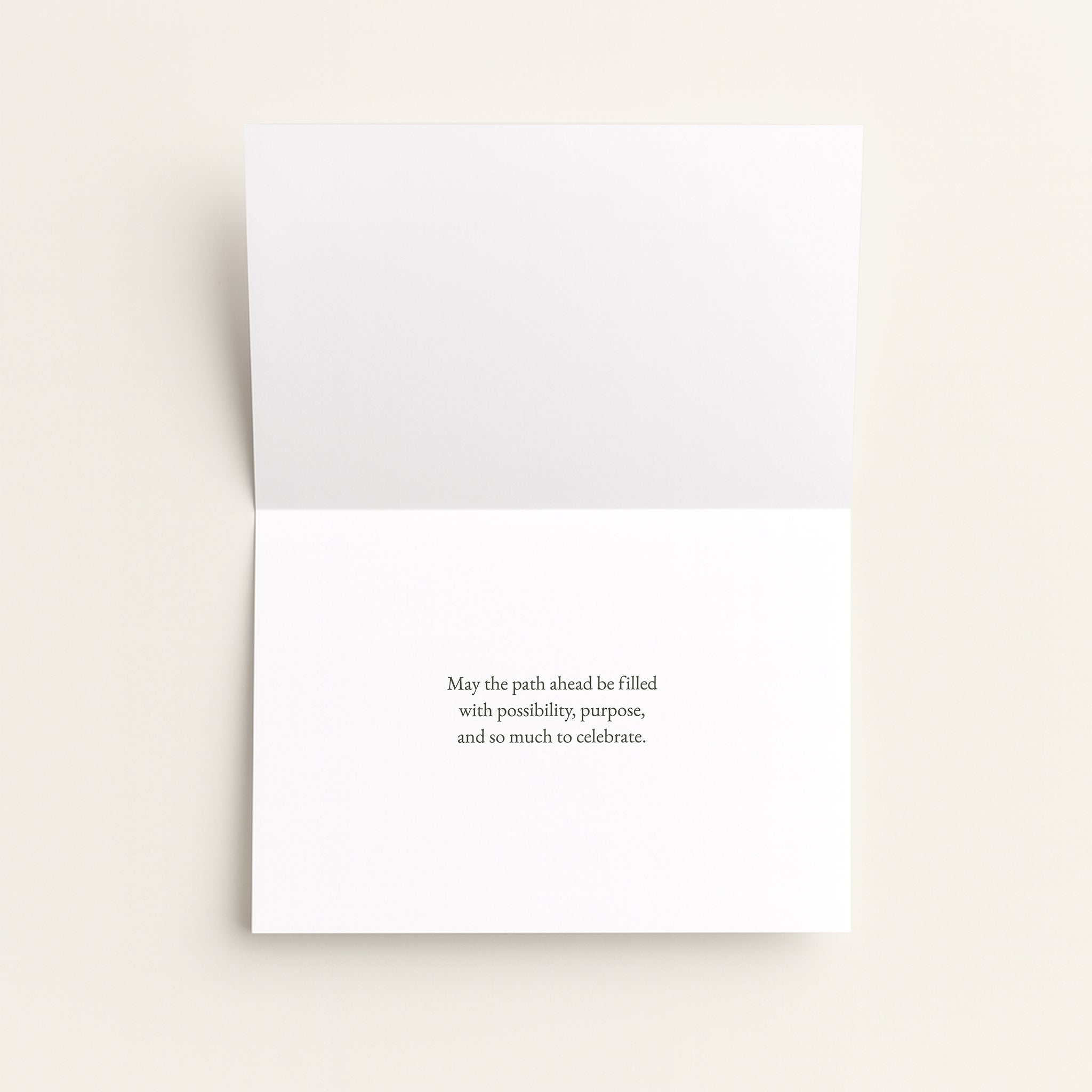 A white greeting card shown open against a light beige background, with a small centered black text message on the lower half.