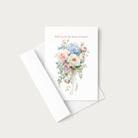 A white greeting card with a watercolor floral bouquet and the text 'Will You Be My Maid of Honor?' in a soft pink font, shown with a matching white envelope on a light gray background.