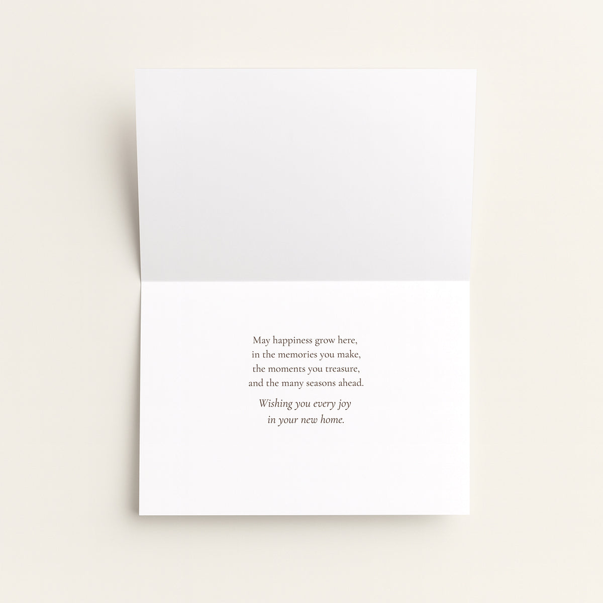 A folded white greeting card with a small centered printed message on the inside, photographed against a light warm beige background.