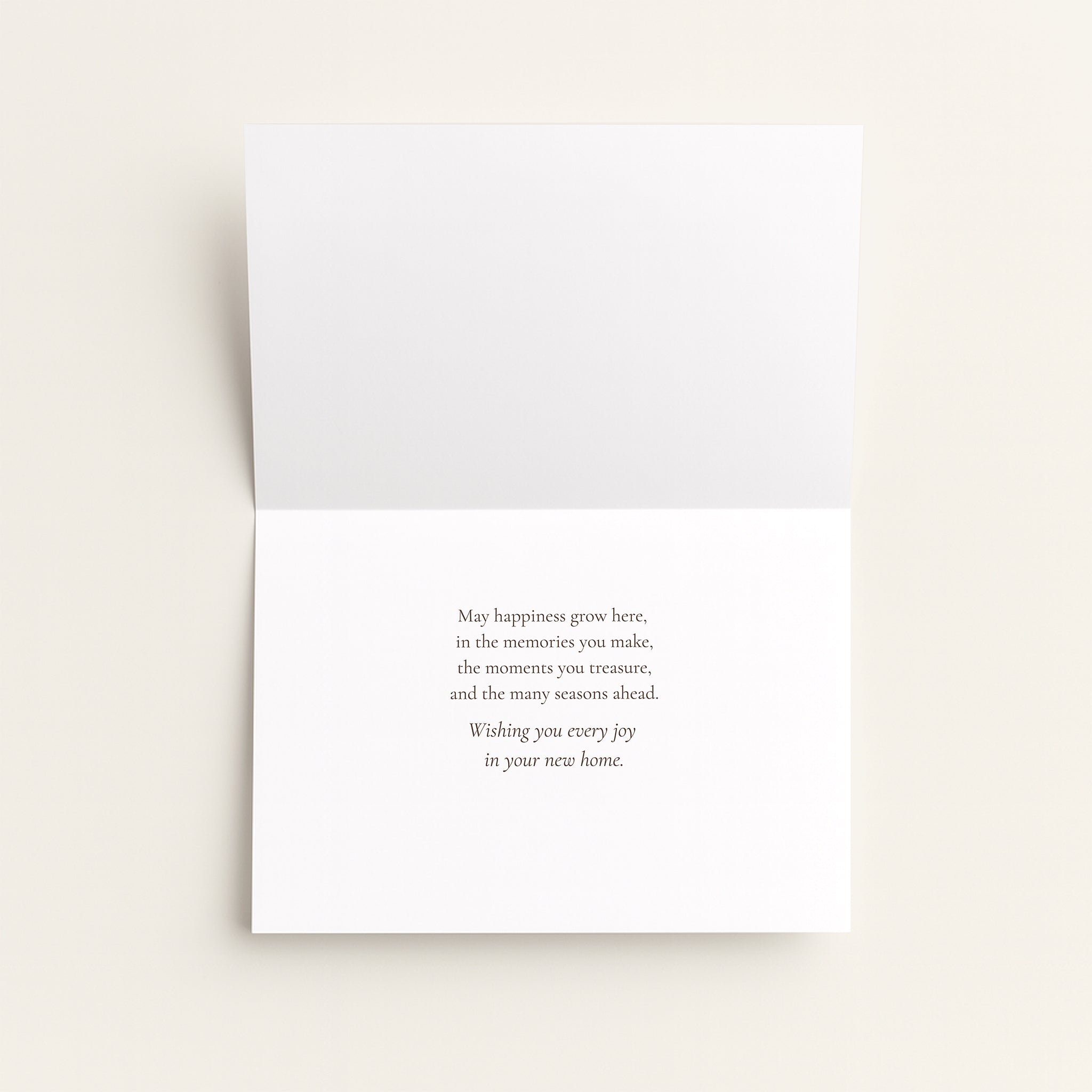 A folded white greeting card with a small centered printed message on the inside, photographed against a light warm beige background.
