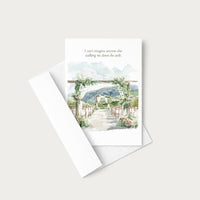 A white greeting card with a watercolor wedding aisle scene and a quote printed at the top, shown with a white envelope on a light warm gray background.