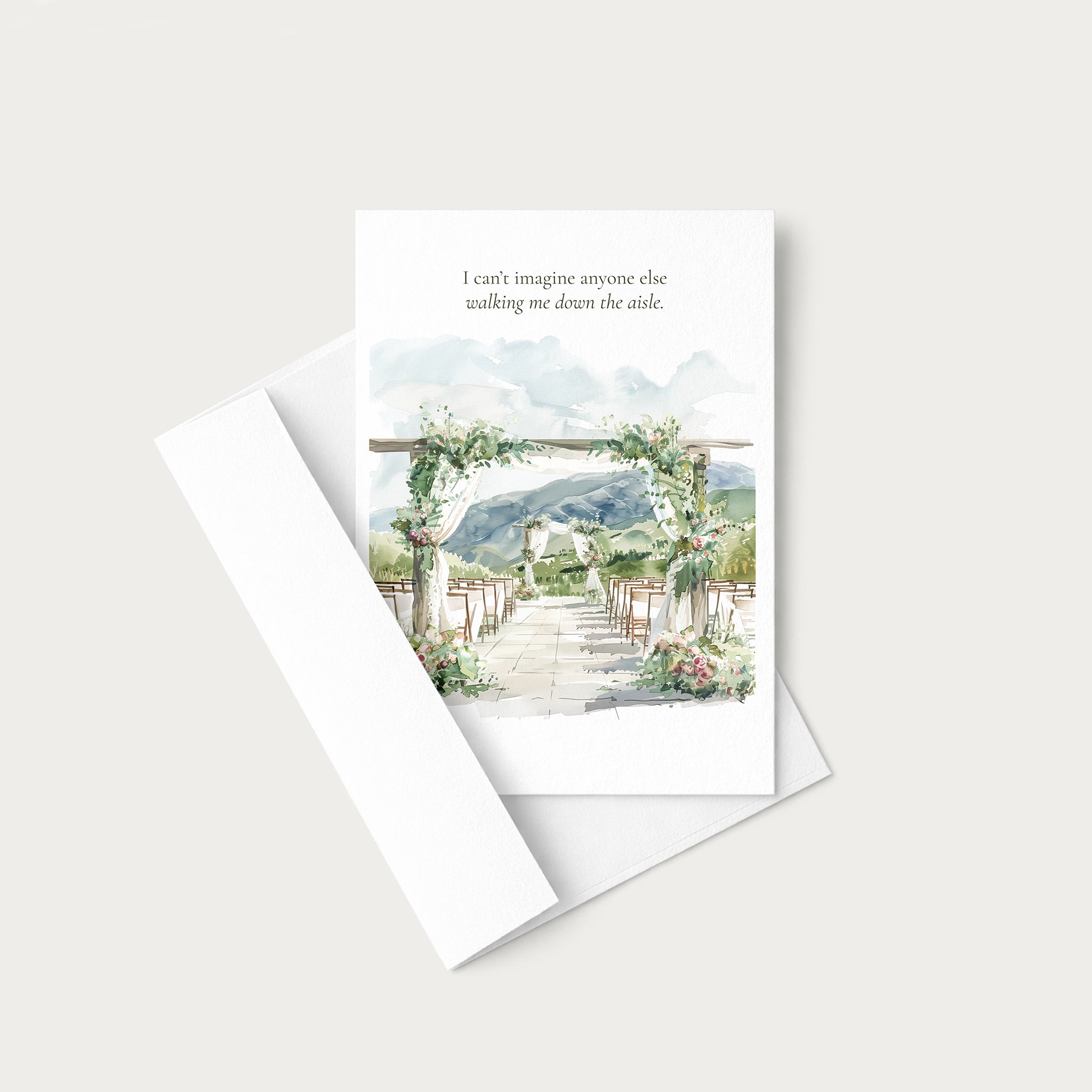 A white greeting card with a watercolor wedding aisle scene and a quote printed at the top, shown with a white envelope on a light warm gray background.