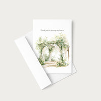A white greeting card with a watercolor illustration of a floral archway and the text 'Thank you for joining our hearts.' shown with a matching white envelope on a light gray background.