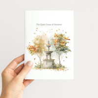 A hand holds a white art print featuring a watercolor illustration of a stone fountain surrounded by autumn trees with orange and yellow leaves. The text at the top reads 'The Quiet Grace of Autumn'.