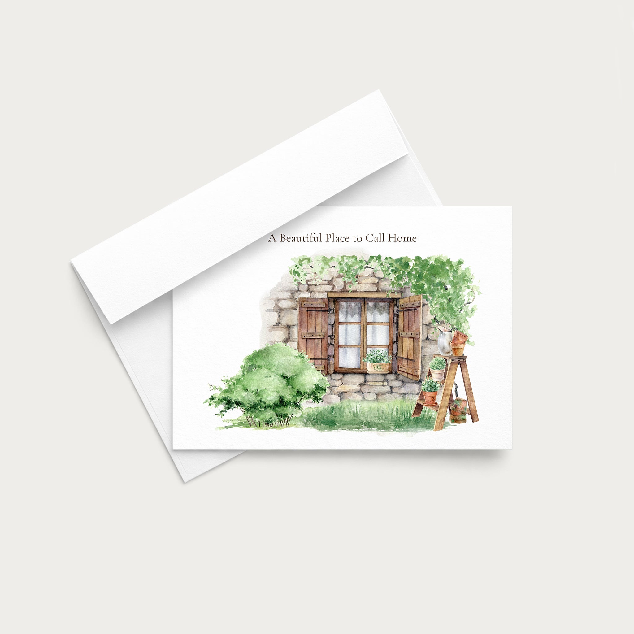 A vertical greeting card with a watercolor illustration of a rustic stone window and greenery, shown with its white envelope on a light gray background.