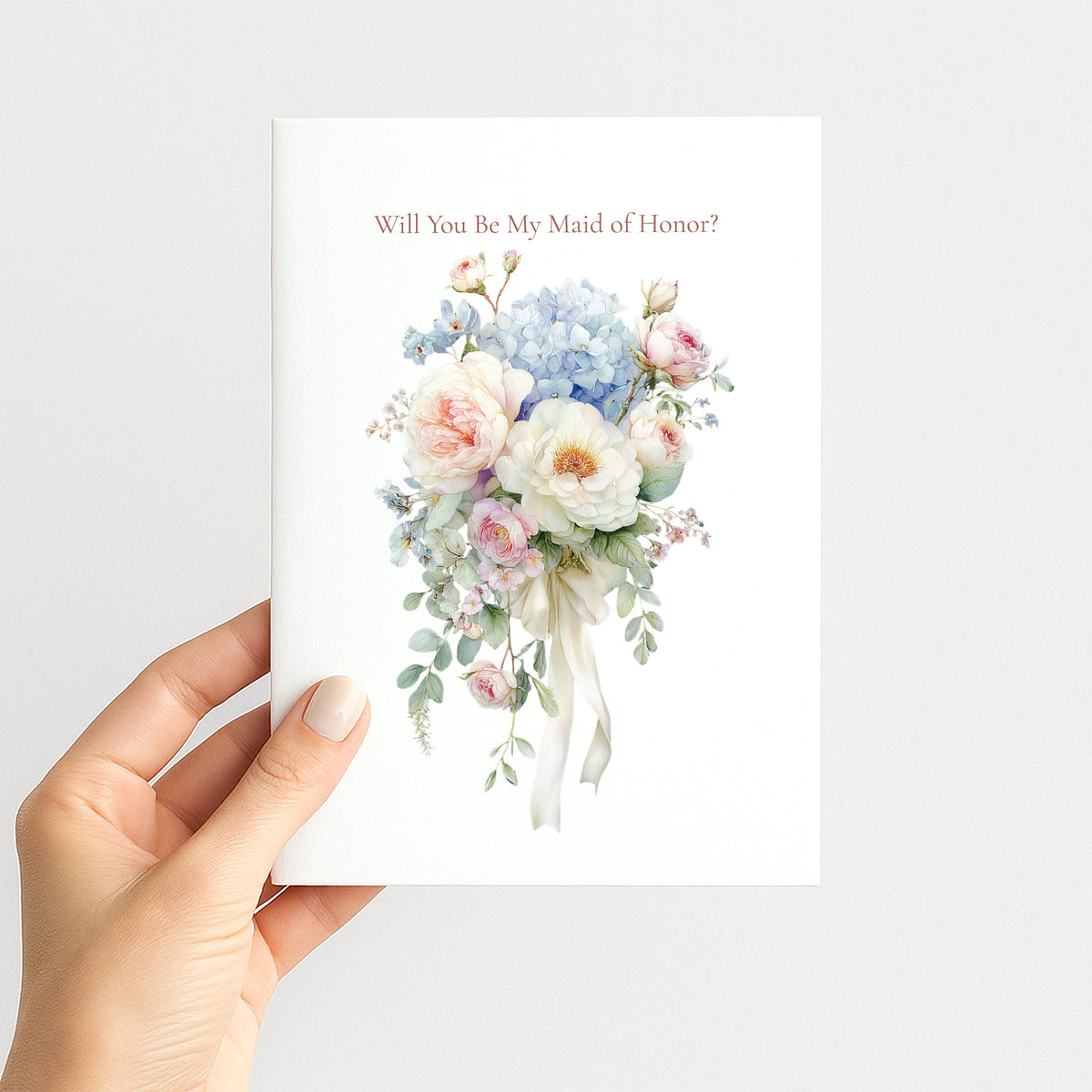 A hand holding a white greeting card that reads 'Will You Be My Maid of Honor?' above a watercolor bouquet of pastel pink, blue, and white flowers with green leaves.