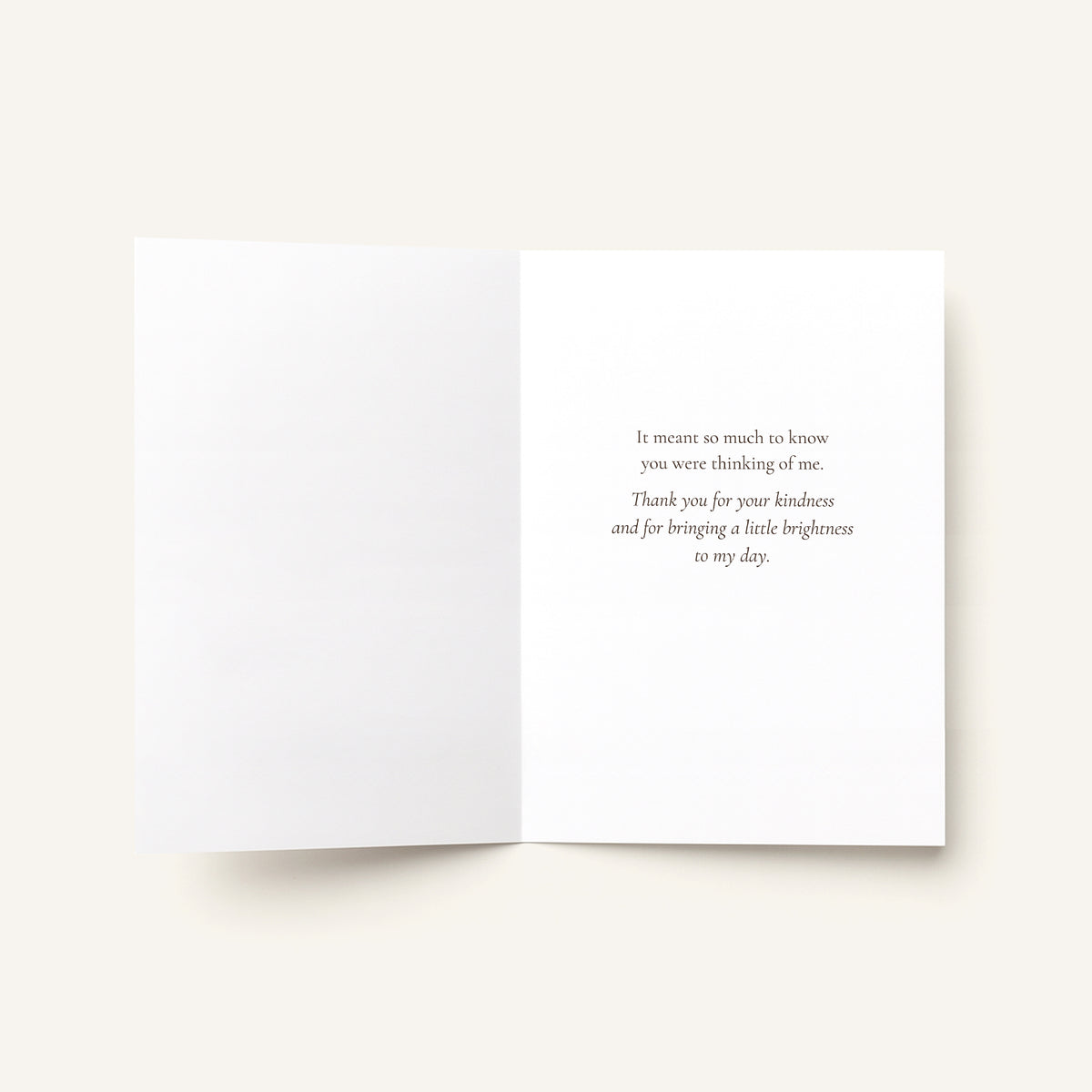 An open white greeting card with a printed quote in a small serif font on the right page, photographed on a light warm beige background.