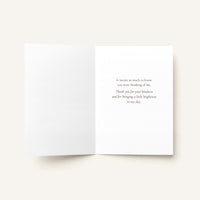 An open white greeting card with a printed quote in a small serif font on the right page, photographed on a light warm beige background.