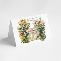 A white A5 greeting card standing upright on its fold, featuring a watercolor illustration of a small wooden picket fence framed by yellow and pink flowers, with the text 'You Have Always Made Life Beautiful' printed above the artwork.