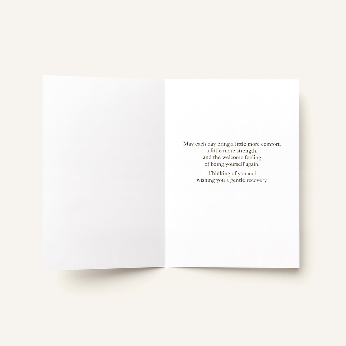 An open white greeting card with a short black printed message on the right panel, photographed on a light warm off-white background.