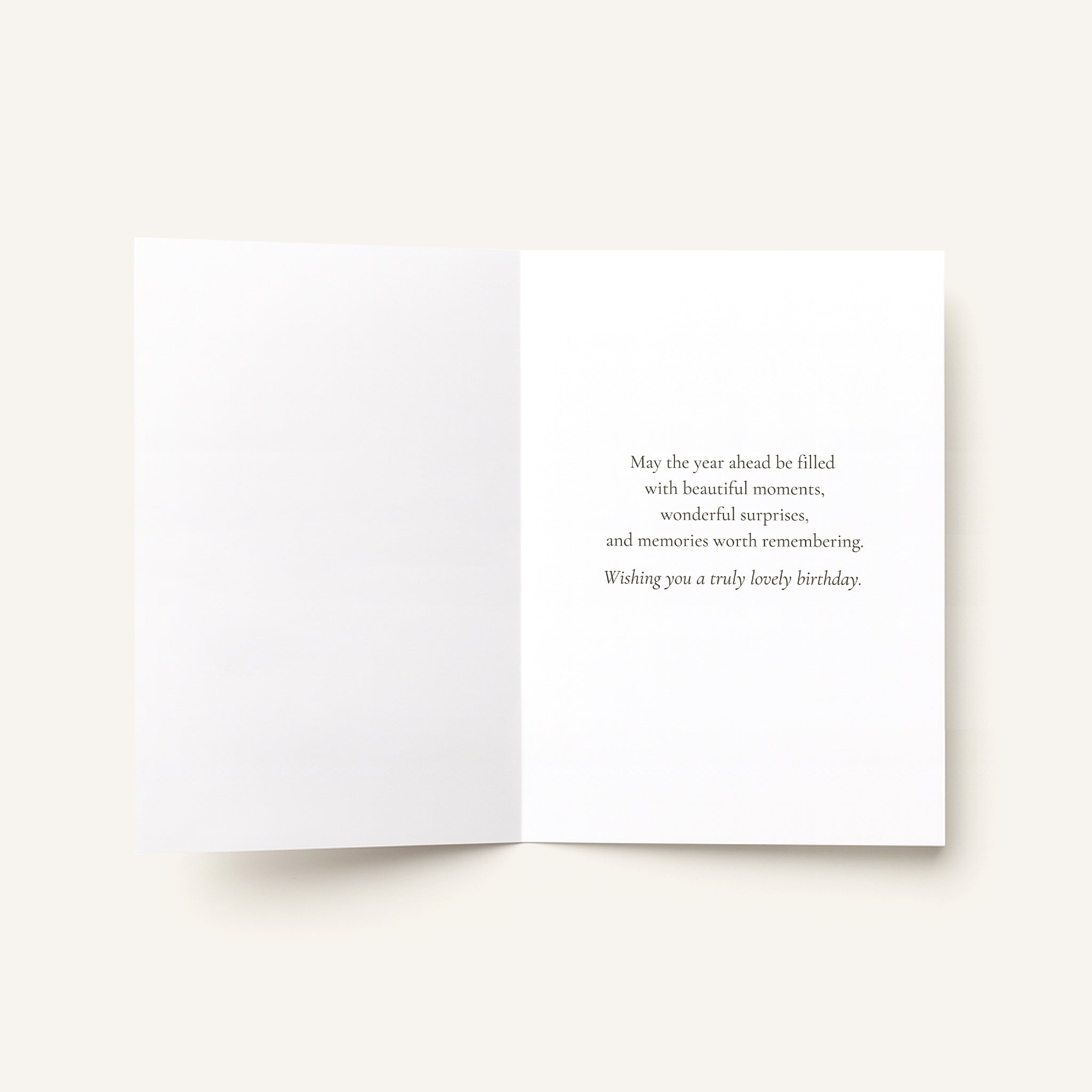 An open white greeting card on a light beige background, with a short printed birthday message in dark gray text on the right panel.