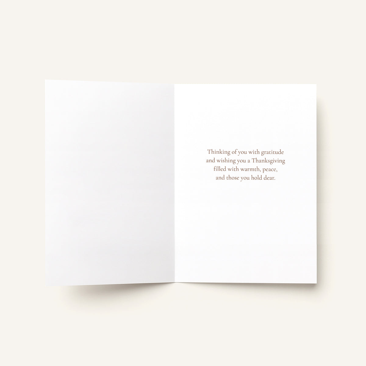 An open white greeting card on a light beige background, with small gray text printed on the right page reading, 'As Thanksgiving and always, I am grateful for the kindness, joy, and friendship you bring to my life.'.
