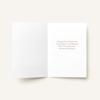 An open white greeting card on a light beige background, with small gray text printed on the right page reading, 'As Thanksgiving and always, I am grateful for the kindness, joy, and friendship you bring to my life.'.