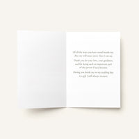 An open white greeting card with elegant gray serif text printed on the right panel, photographed against a warm off-white background.