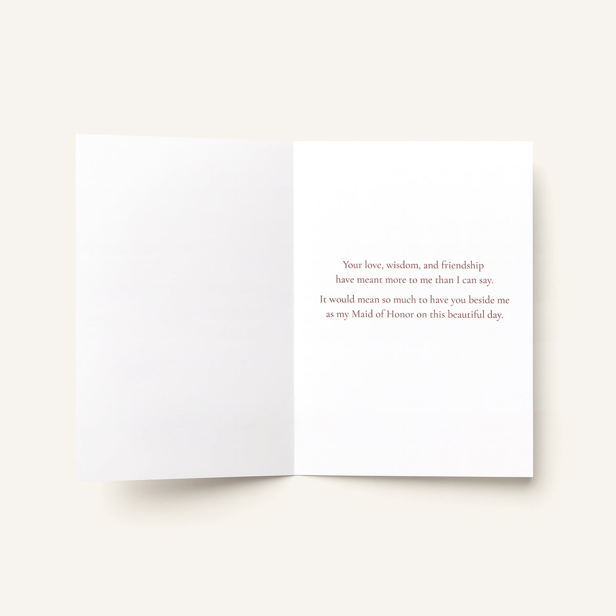 An open white greeting card with a printed message in small gray text on the right panel, photographed on a light warm beige background.