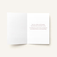 An open white greeting card with a printed message in small gray text on the right panel, photographed on a light warm beige background.