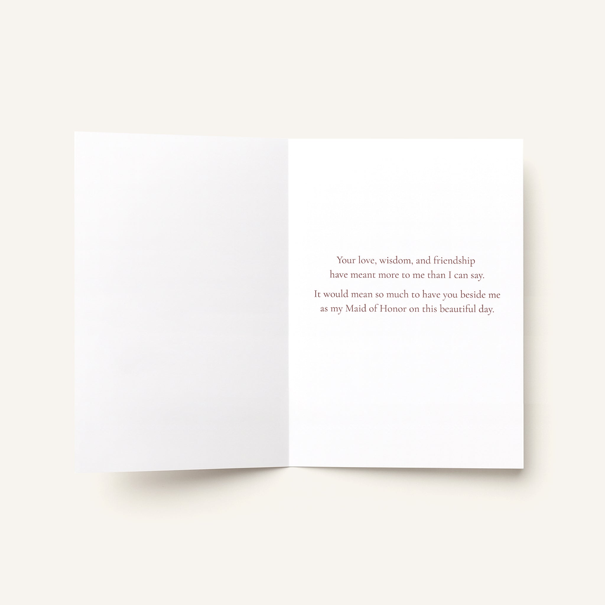An open white greeting card with a printed message in small gray text on the right panel, photographed on a light warm beige background.