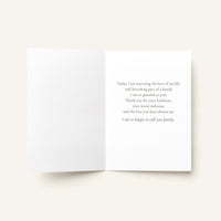 An open white greeting card with a printed wedding message in black serif text on the right panel, photographed on a light warm beige background.