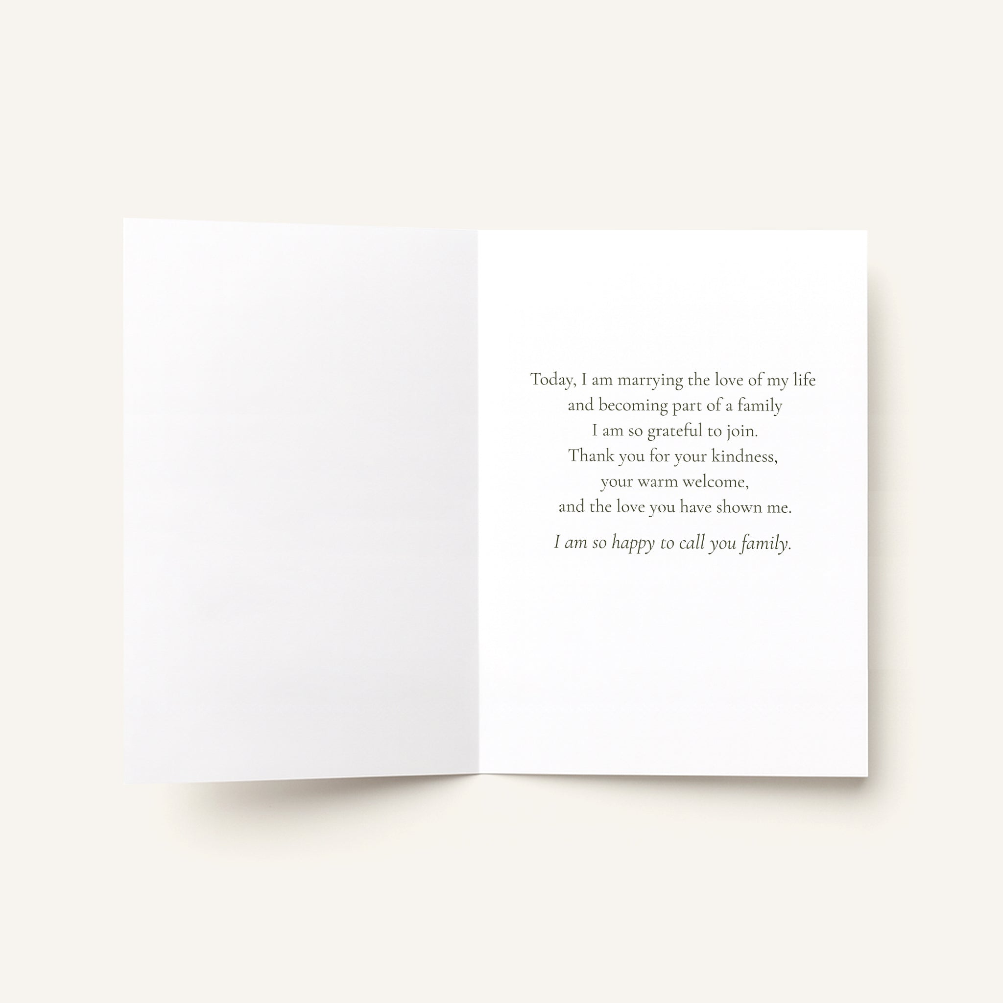 An open white greeting card with a printed wedding message in black serif text on the right panel, photographed on a light warm beige background.
