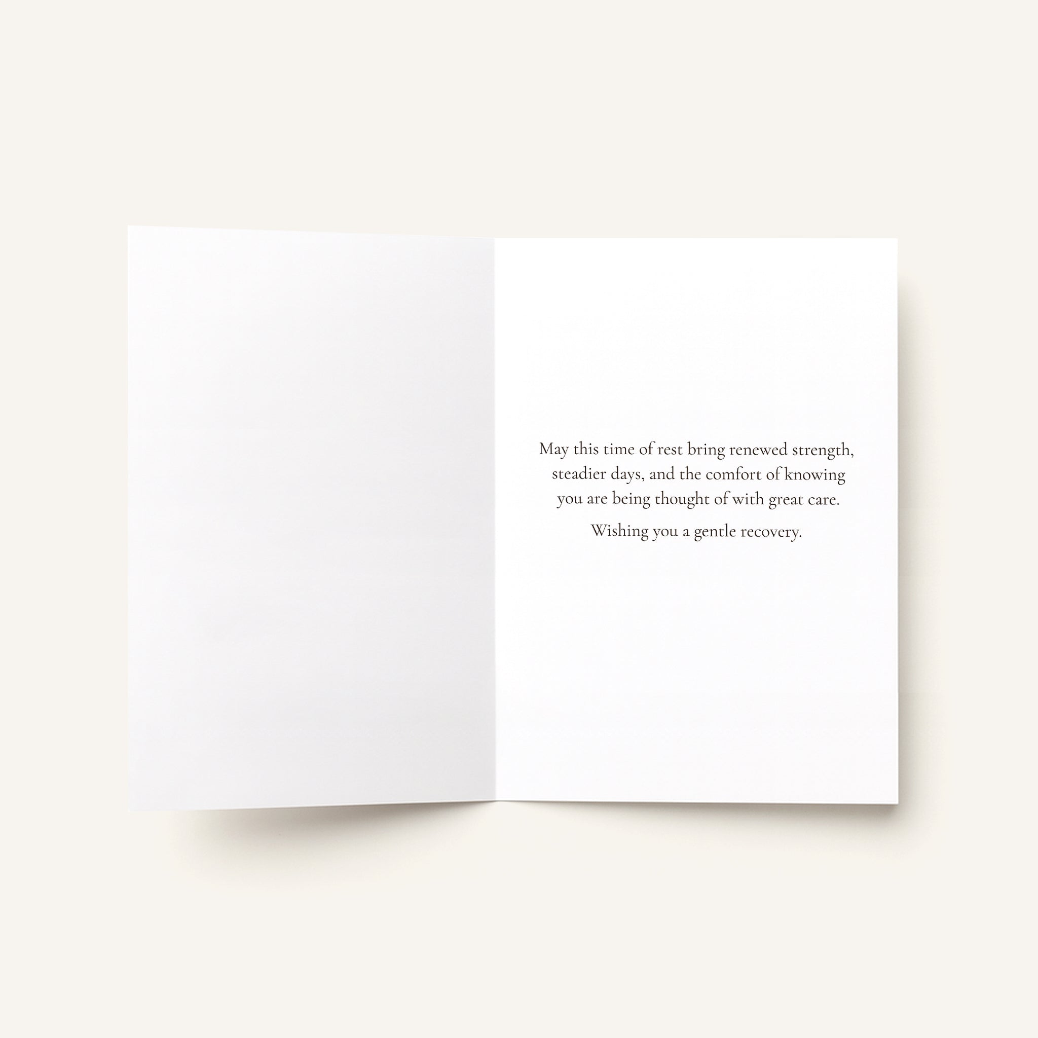 An open white greeting card with a printed birthday message in dark gray text on the right panel, photographed on a light warm beige background.