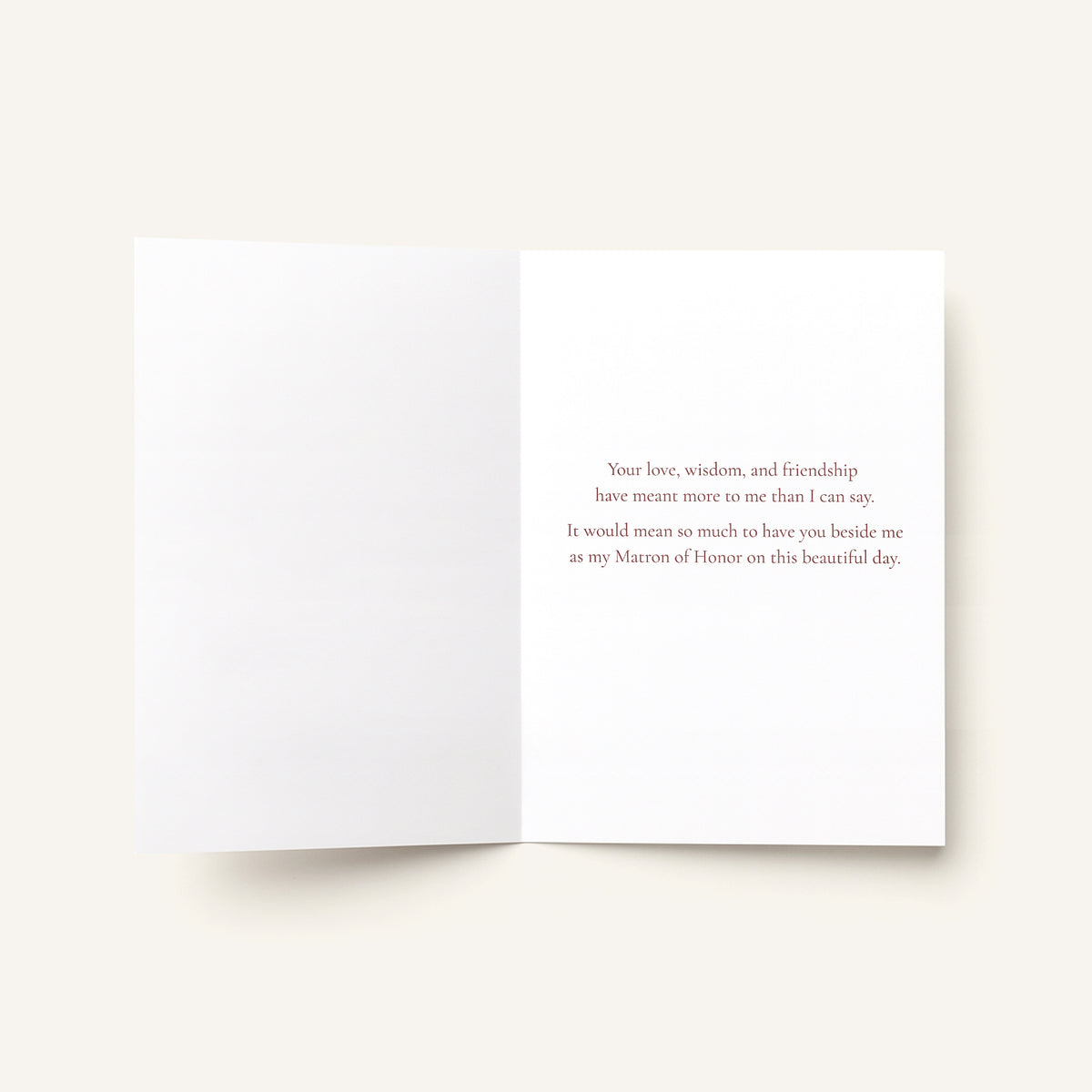 An open white greeting card with a printed message in small gray text on the right panel, photographed on a light warm beige background.