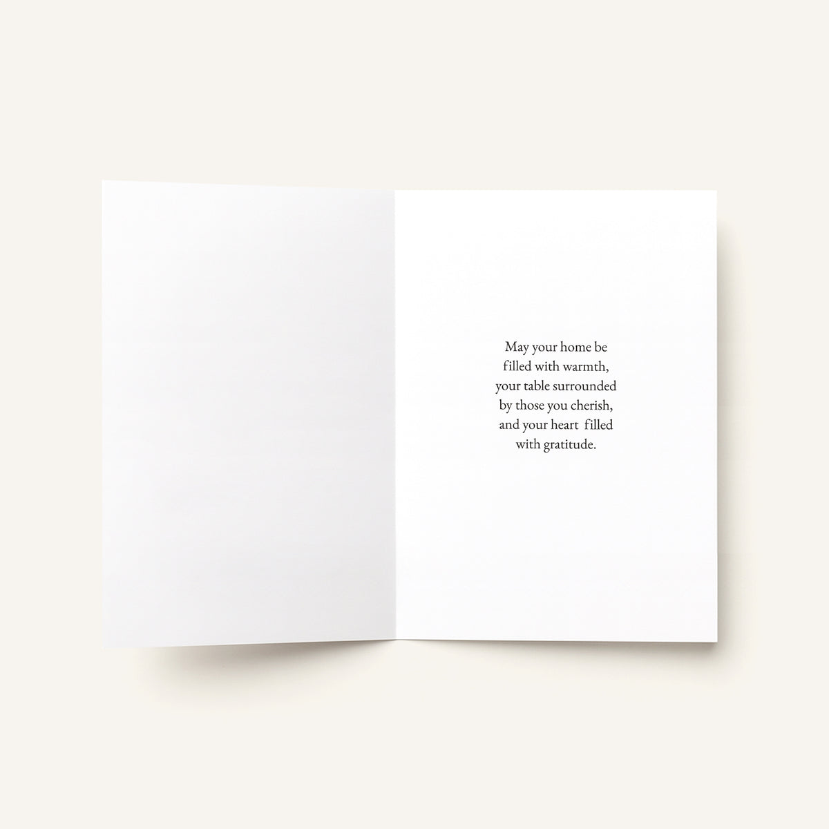 An open white greeting card with a warm message printed in black serif text on the right panel, photographed on a light warm beige background.