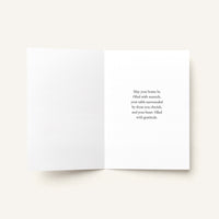 An open white greeting card with a warm message printed in black serif text on the right panel, photographed on a light warm beige background.