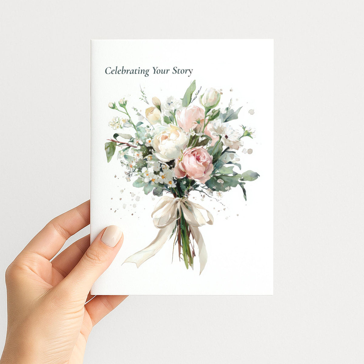 Hand holding Celebrating Your Story anniversary card featuring a watercolor bouquet tied with a cream ribbon.