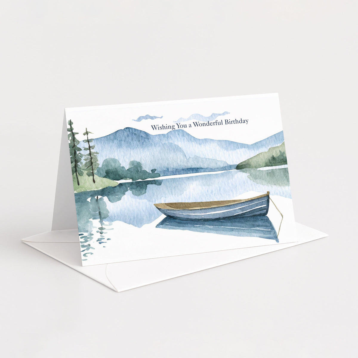 Landscape birthday card with a blue mountain lake and rowboat resting on a white envelope.